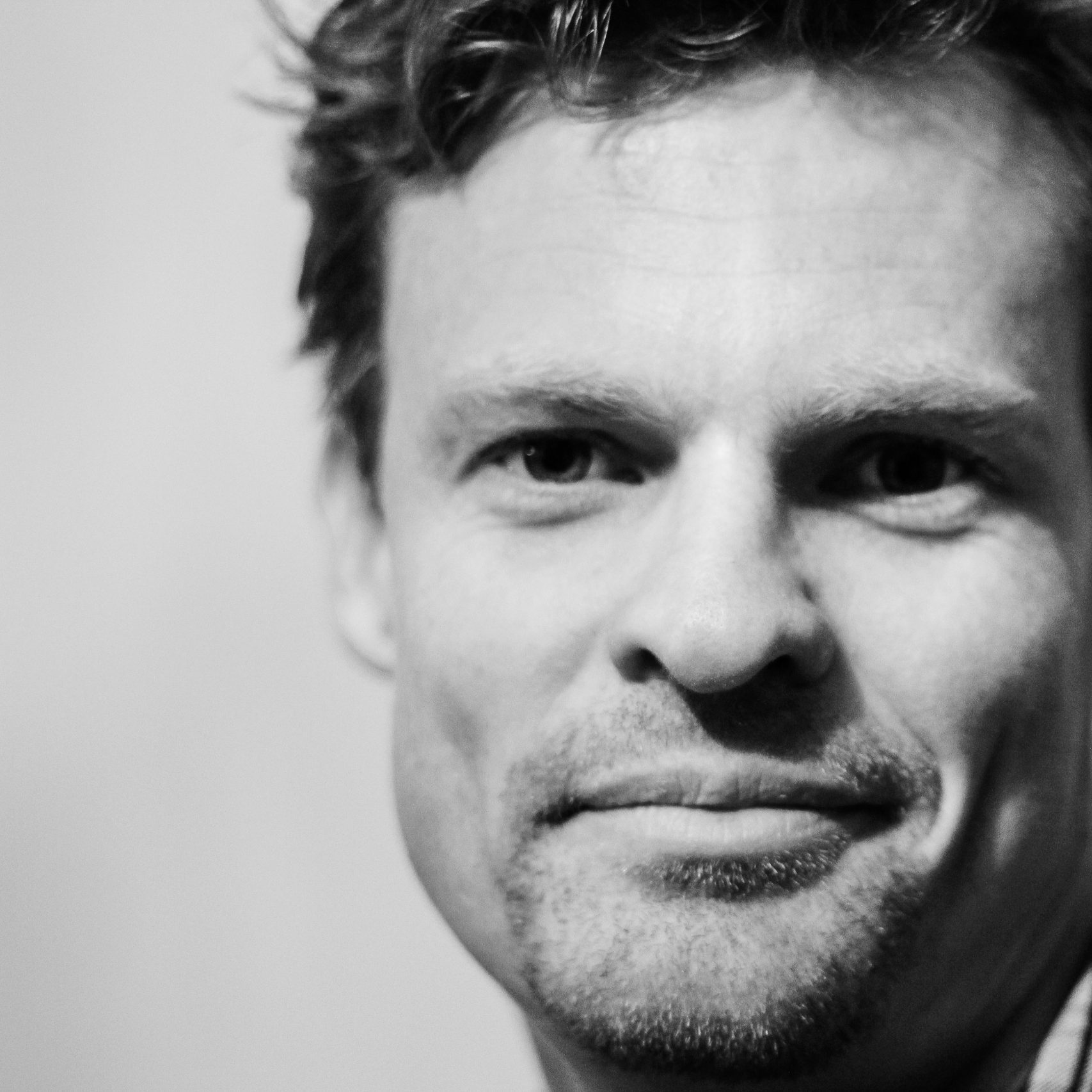 Close-up black and white portrait showcasing a smiling man with facial hair.