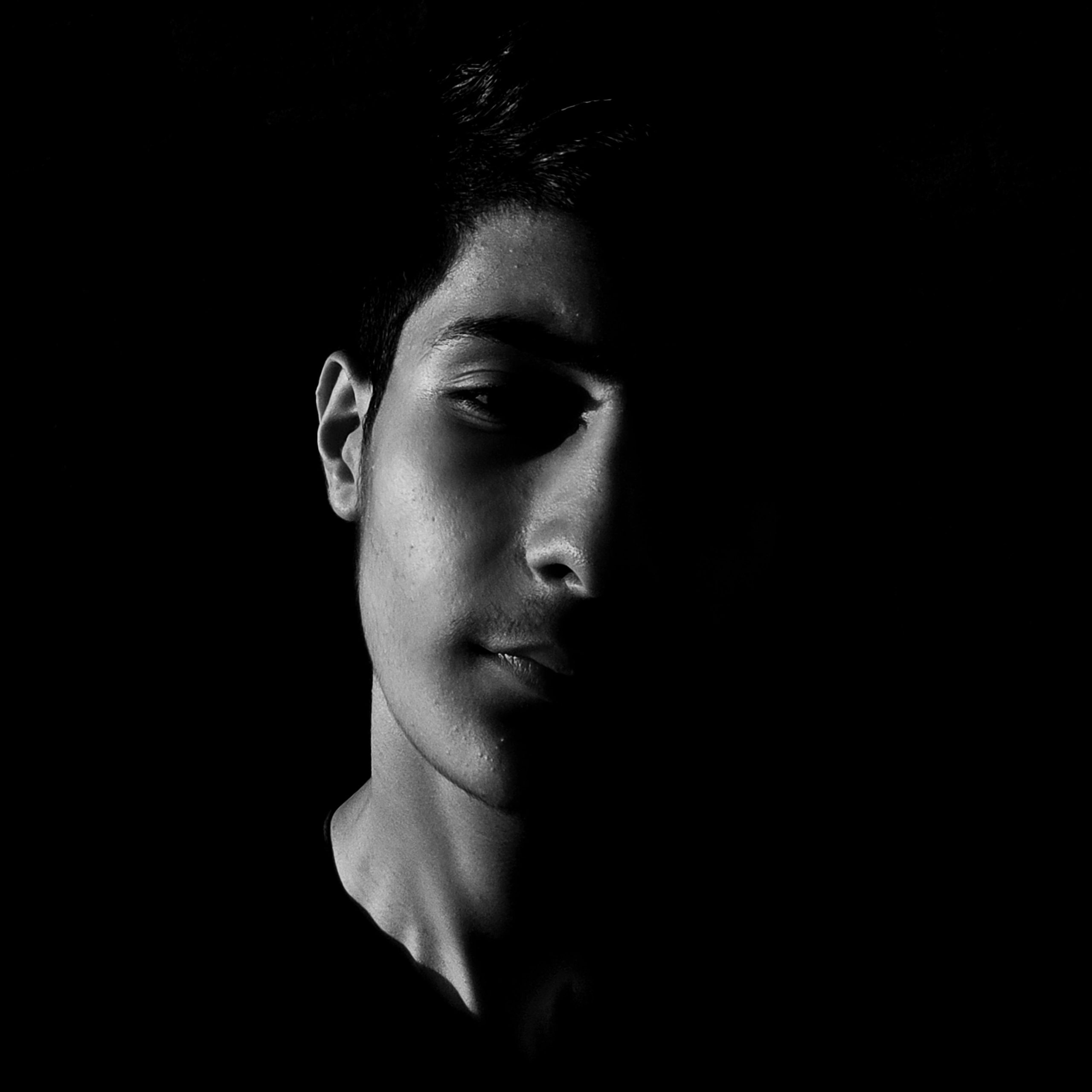 Dramatic black and white portrait of a man with half face in shadow, capturing a mysterious mood.